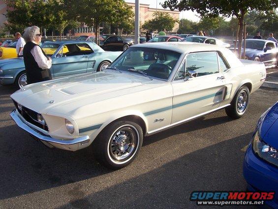 White 1967 Ford Mustang coupe with blue side stripes, chrome bumper, and aftermarket wheels