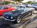 2002 Ford Mustang - A classic dark green convertible is parked in a lot next to a red coupe, with a man standing behind it.