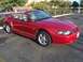 2002 Ford Mustang - A red 2002 Ford Mustang convertible is parked in a lot with trees and buildings in the background.