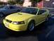 2002 Ford Mustang - A yellow convertible Mustang is parked next to a classic silver coupe, both appearing to be at an outdoor event.