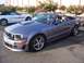 2002 Ford Mustang - A gray convertible Mustang with racing stripes is parked in a lot next to a white convertible Mustang.