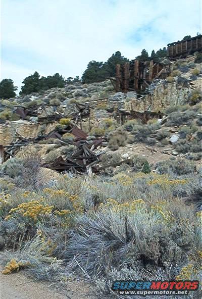 Old wooden mine buildings and debris on a rocky hillside with scrub brush