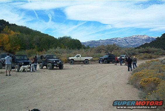 Several off-road vehicles parked on a dirt road with mountains in the background