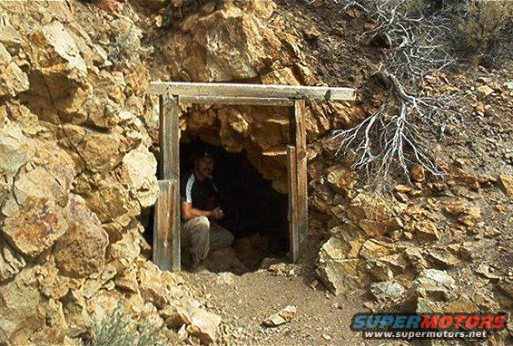 Man crouched at the entrance of a mine shaft in a rocky hillside
