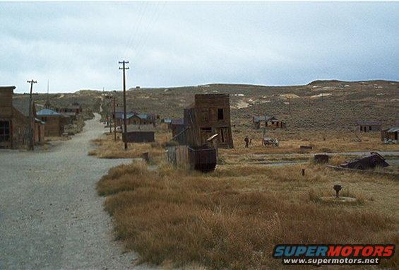 Ghost town street with wooden buildings and dry vegetation under a cloudy sky