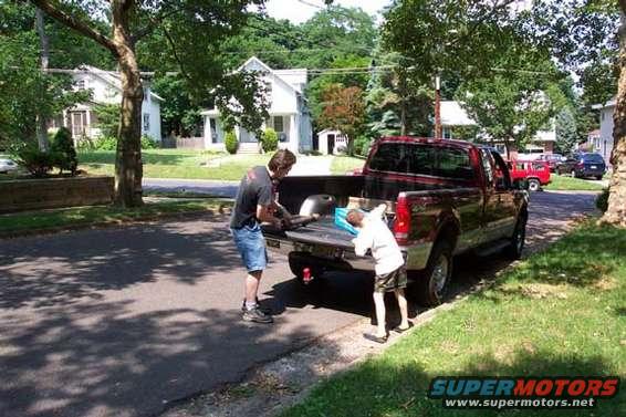 Red pickup truck with tailgate down, two people loading items into the bed