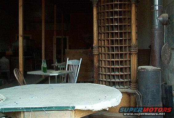 Old building interior with tables, chairs, a wood stove, and a large pigeonhole organizer