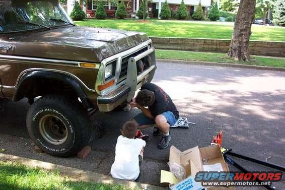 Brown 1978 Ford Bronco front end with a brush guard, two people working on it