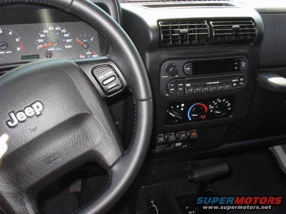 Jeep TJ interior showing steering wheel with cruise control buttons, dashboard gauges, and center console with radio and climate controls