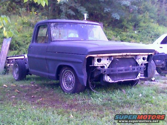 Dark blue Ford truck chassis with custom wire wheels, missing front grille and bumper