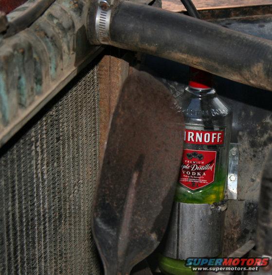 Engine bay detail showing radiator, hose, shovel, and a bottle of Smirnoff vodka