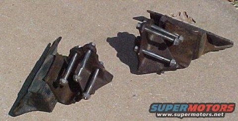 Two metal engine mounts with bolts attached, resting on concrete
