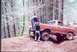 1976 Ford F-100 - Two people are working on an orange Ford pickup truck as it navigates a dirt path in a wooded area.