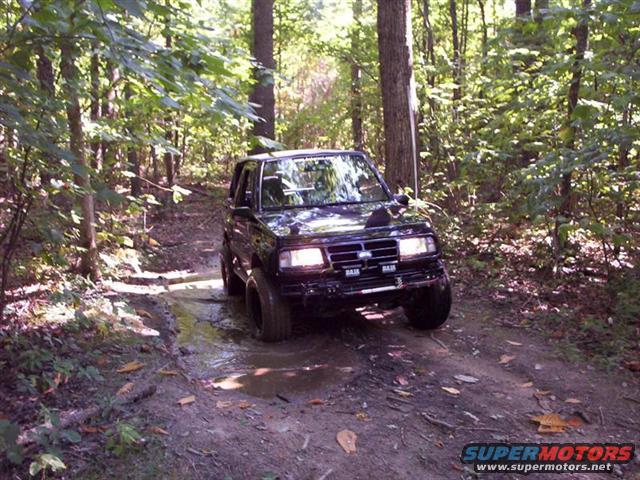 1996 Chevrolet Tracker driving through mud on a wooded path