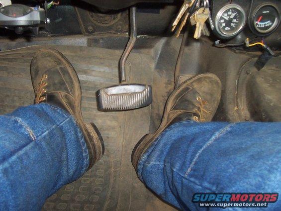 Driver's feet in jeans and boots on brake and gas pedals inside a vehicle. Keys hang from the ignition