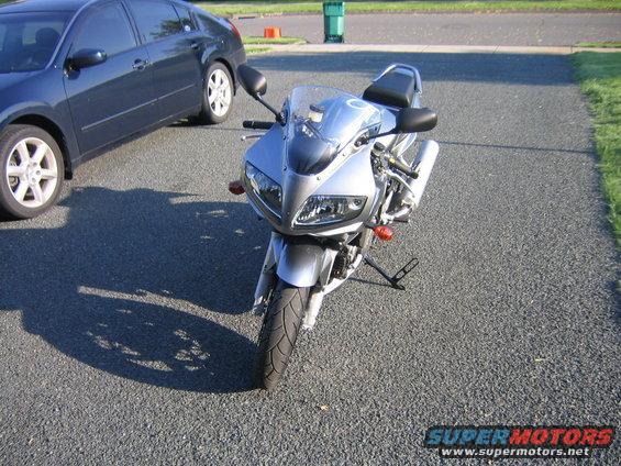 Front view of a silver sport motorcycle parked on asphalt next to a dark blue sedan