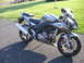 2006 Suzuki SV1000S - A silver 2006 Suzuki SV1000S motorcycle is parked on a paved surface, viewed from the front three-quarter angle.