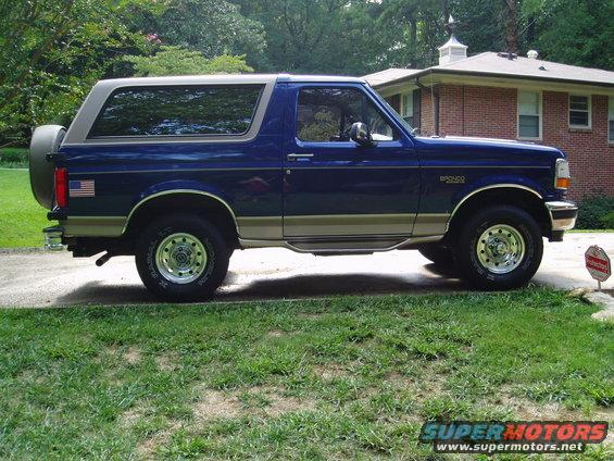 Side view of a blue and tan 1996 Ford Bronco with a spare tire on the rear