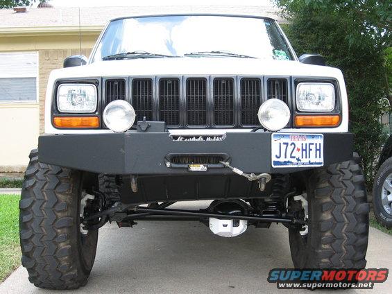 Front view of a white Jeep Cherokee XJ with a custom bumper, winch, and large off-road tires. Texas license plate J72-HFH is visible