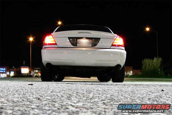 Rear view of a white sedan parked at night. Taillights are illuminated