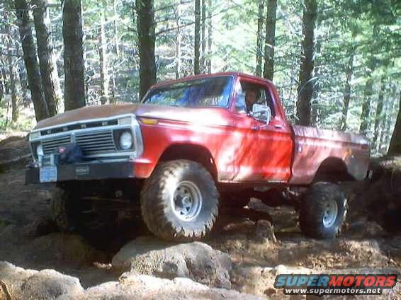 Red Ford pickup truck with a rusty hood, lifted suspension, and large off-road tires, angled to the front