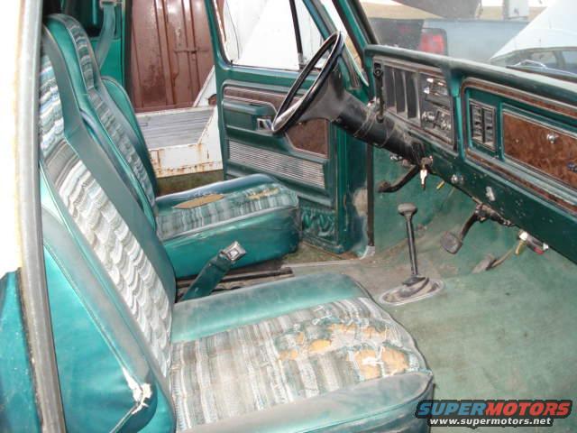 Interior of a green truck with worn striped seats, dashboard, and steering wheel