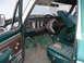 1979 Ford Bronco - The interior of this 1979 Ford Bronco shows its dashboard, steering wheel, and a torn green striped driver's seat.