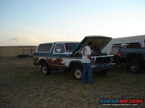 1978 Ford Bronco with hood open, man checking engine. Another truck is parked behind it