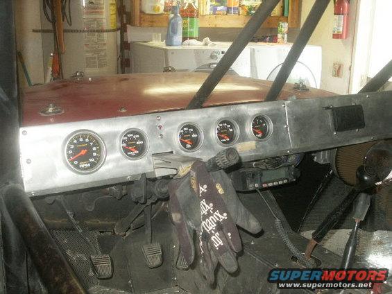 Custom dashboard with multiple gauges, floor pedals, and work gloves hanging from the steering column