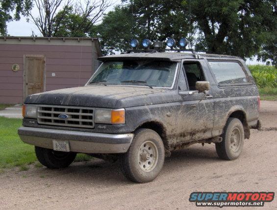 Black 1987 Ford Bronco with off-road lights, covered in mud