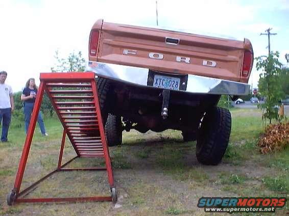 Brown Ford truck rear view, chrome bumper, red ramp, two people standing