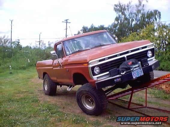 Orange pickup truck with lifted suspension on red ramps. License plate reads TTC 028