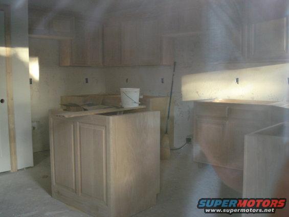 Kitchen under construction with unfinished cabinets and a bucket