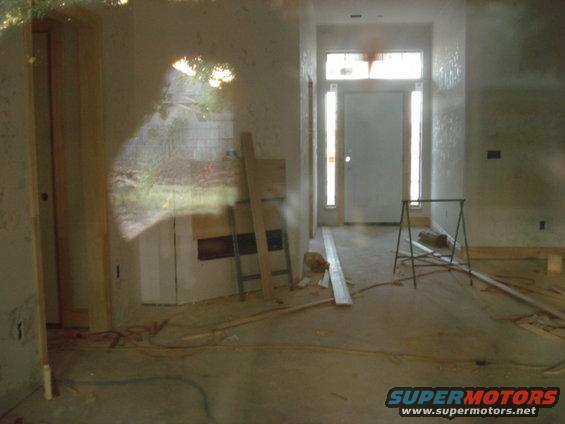 Interior of a house under construction with a door and windows visible, along with ladders and building materials