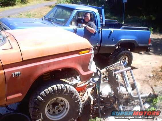 Orange 1976 Ford F-100 front fender and wheel next to a blue pickup truck with a man driving