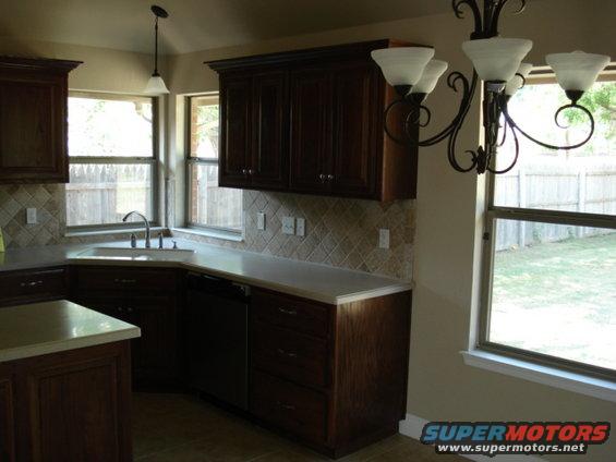 Kitchen interior with dark wood cabinets, sink, and window overlooking a backyard