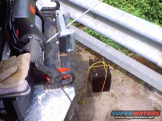 Battery tied with yellow rope next to a winch and a glove