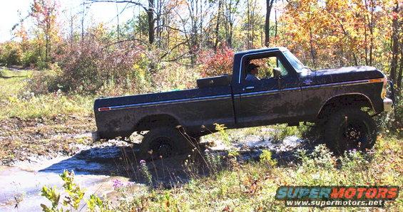 Dark pickup truck with lifted suspension driving through mud and brush