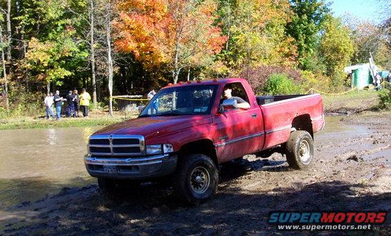 Red Dodge Ram pickup truck driving through mud and water with fall foliage in the background