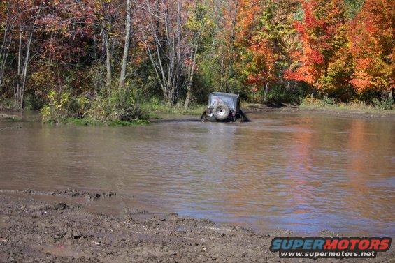 Off-road vehicle stuck in water with fall foliage in background