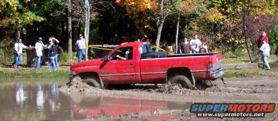 Red pickup truck stuck in mud with people watching