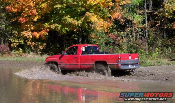 Red pickup truck splashing through a muddy puddle with fall foliage in the background