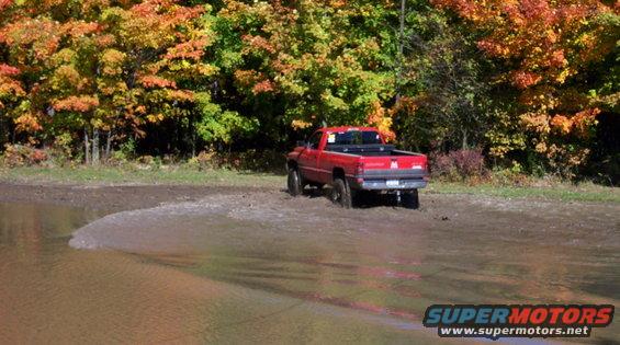 Red pickup truck stuck in mud with fall foliage in the background