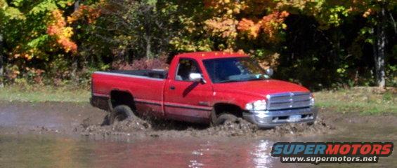 Red pickup truck driving through mud, front quarter view