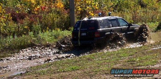 Black SUV splashing through a muddy trail with trees in the background