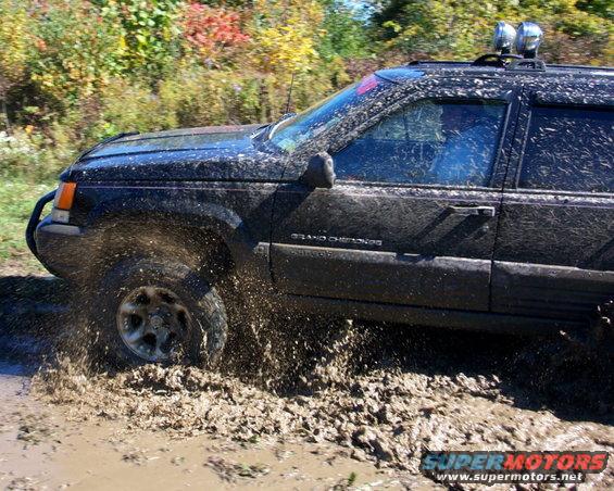Black Jeep Grand Cherokee splashing through mud, side view