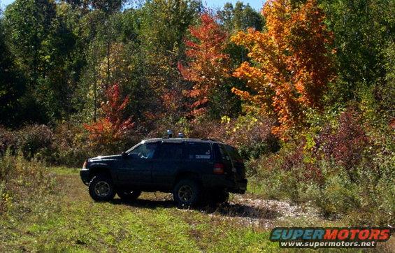 Dark SUV parked on a dirt path with fall foliage in the background