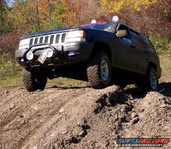 Black Jeep Grand Cherokee with off-road tires climbing a dirt hill