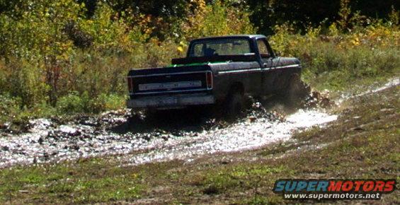 Black pickup truck in mud, rear view. Appears to be a 1970s Ford F-Series