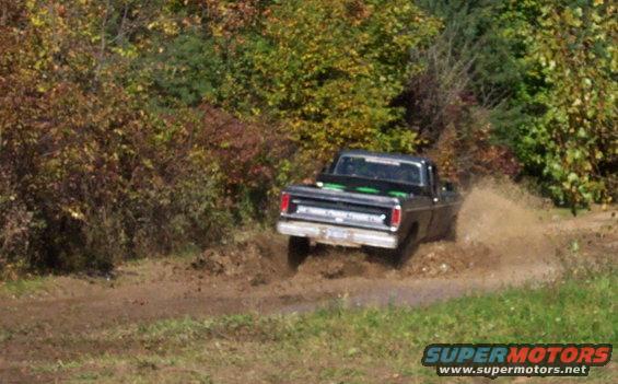 Rear view of black 1970s pickup truck splashing through mud